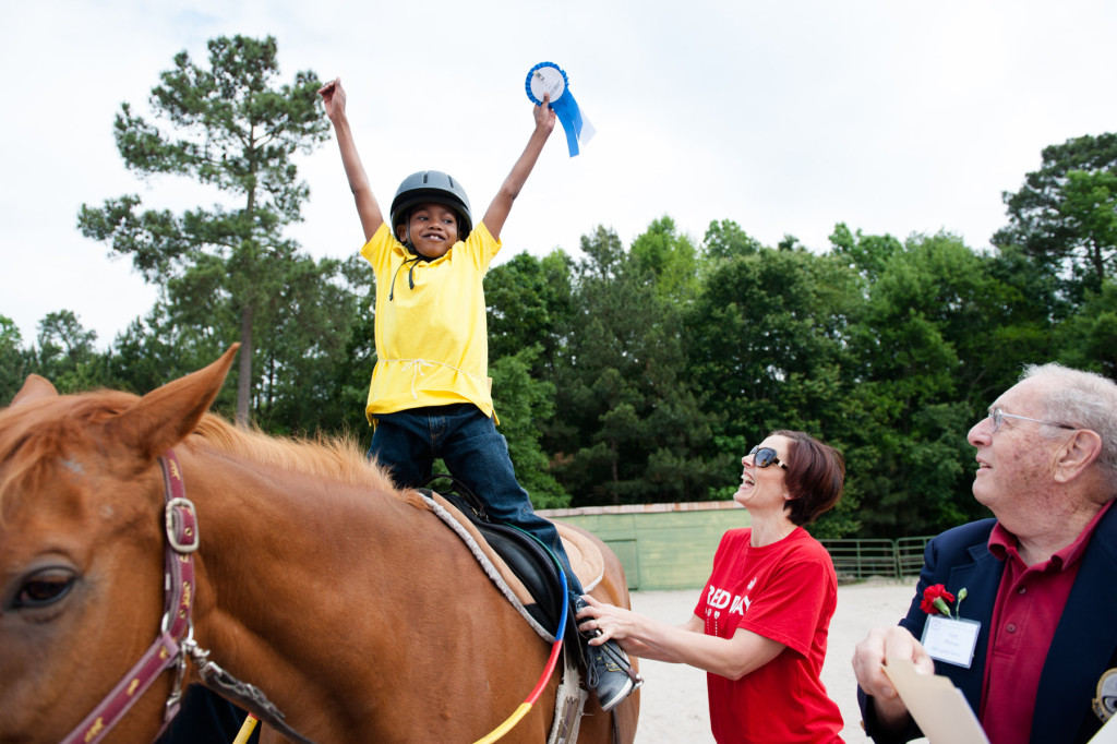 Volunteer Claire Slyman laughs as 6-year-old Daryl Green smiles and celebrates his ribbon after placing during a Prancing Horse show at Muddy Creek Farm off Trails End Road on Thursday, May 14, 2015 in Whispering Pines, North Carolina.