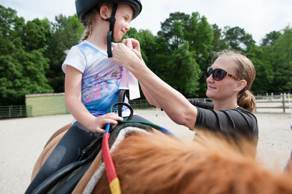 Tabitha Justin, Emmylyn's mother, hangs the award ribbon from her daughter's shirt to show off after placing during a Prancing Horse show at Muddy Creek Farm off Trails End Road on Thursday, May 14, 2015 in Whispering Pines, North Carolina.