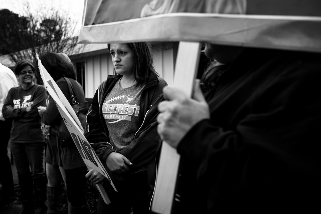 Seventeen-year-old  Pinecrest Junior Kylie Kreitlow holds a poster as she stands with other people in support of Chris Metzger, the head football coach of Pinecrest High School's football team, during a peaceful demonstration outside of the Moore County Education Building off 15-501 on Friday, December 18, 2015 in Carthage, North Carolina.