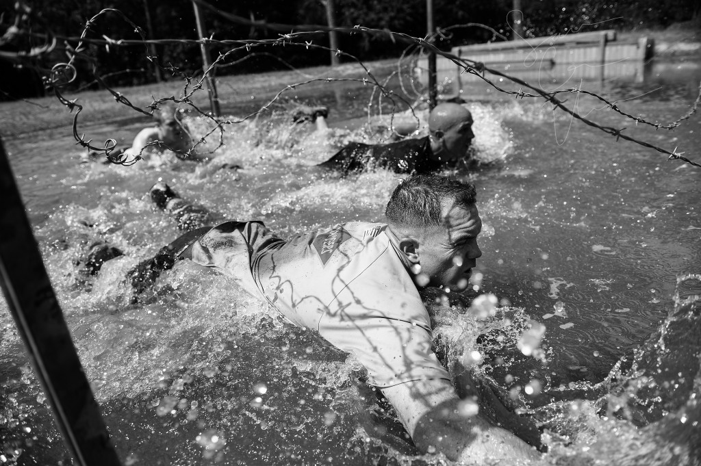 Teams in the competitor's wave of the Muddy Nick 10K crawl through a water hazard, and under lines of barbed-wire, during the Special Operators Challenge at the Carolina Horse Park on Saturday, May 30, 2015 in Raeford, North Carolina.